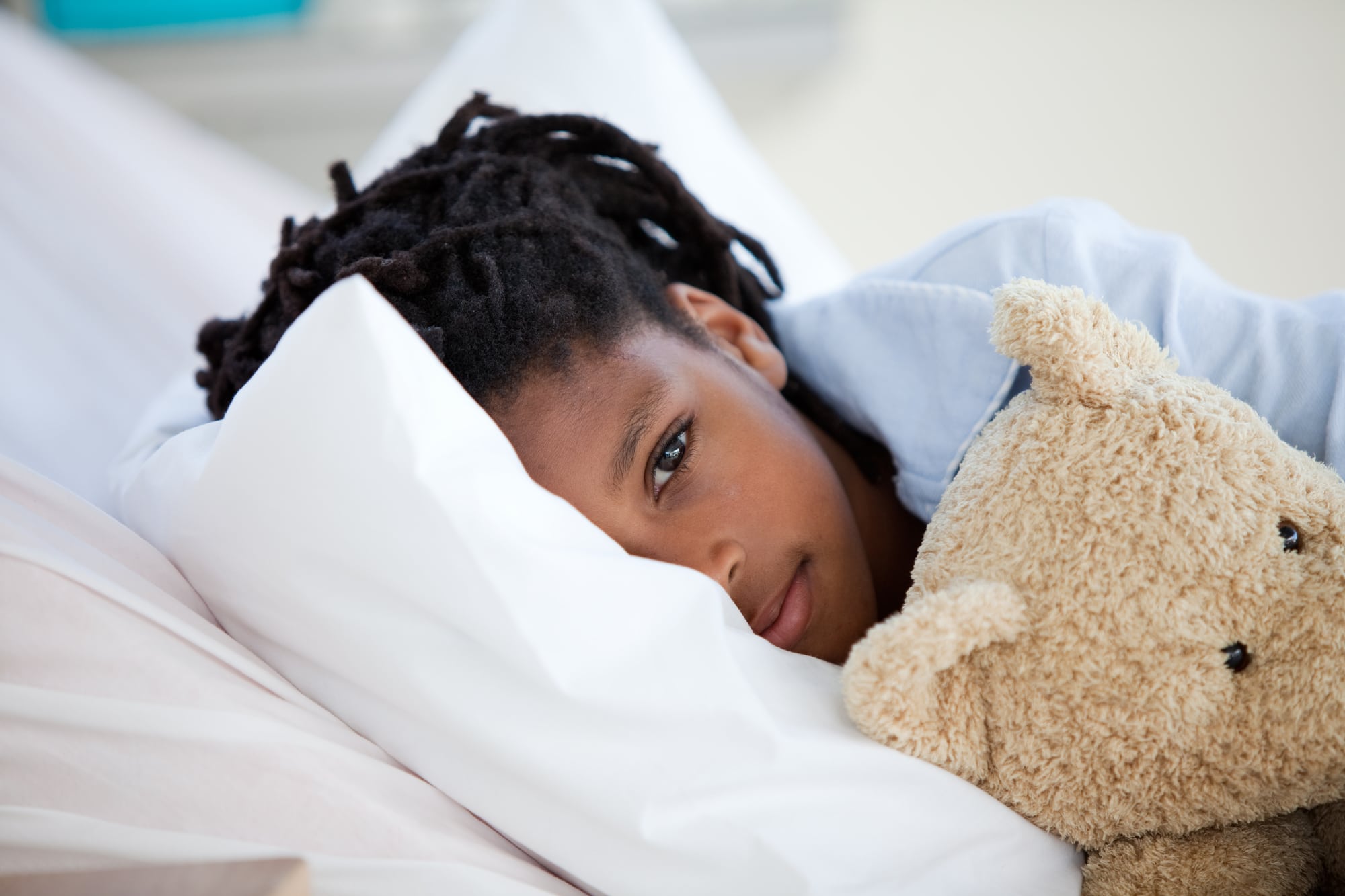 sick child lying in bed cuddling with a teddy bear