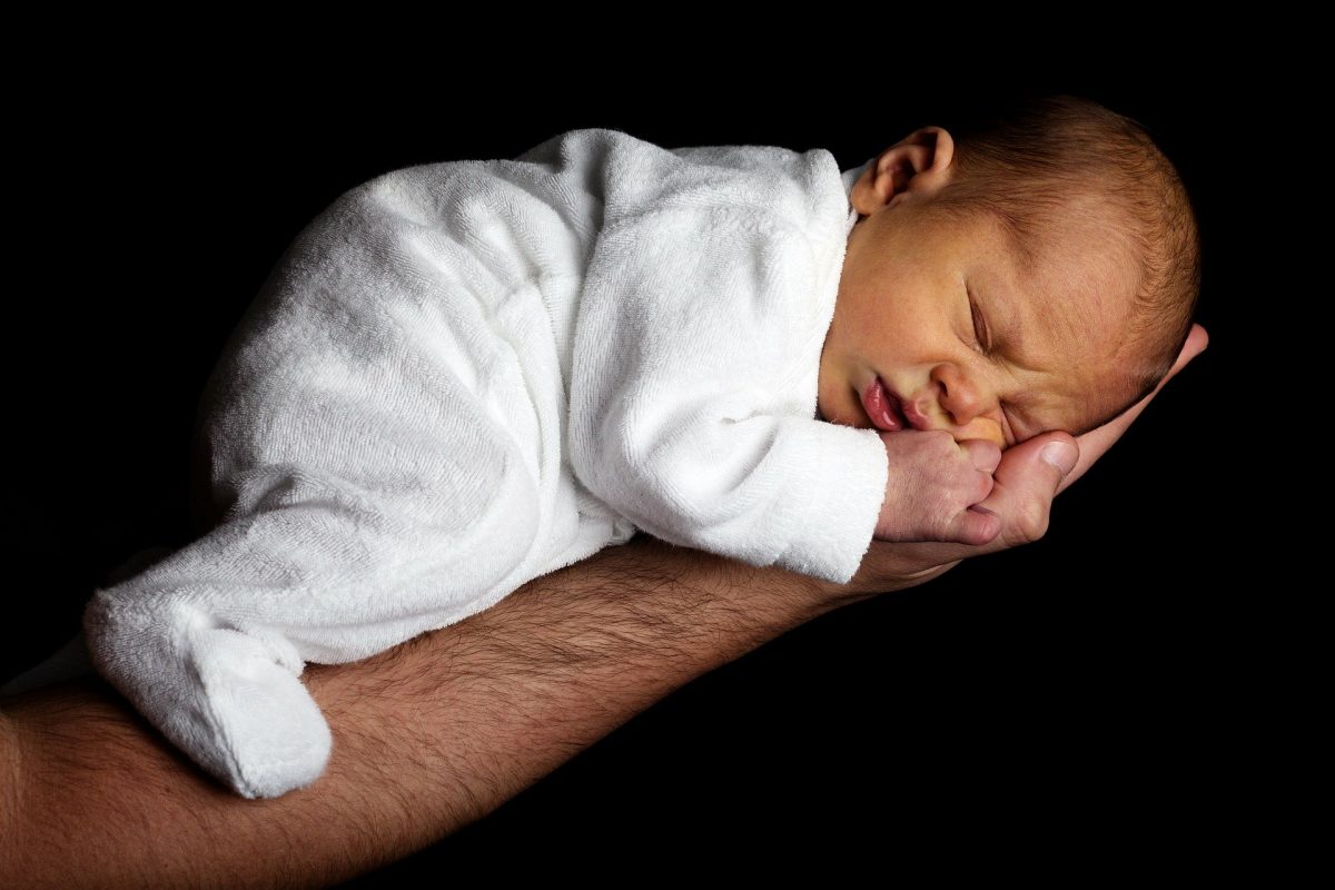 A newborn sleeping on their side in their father's arms