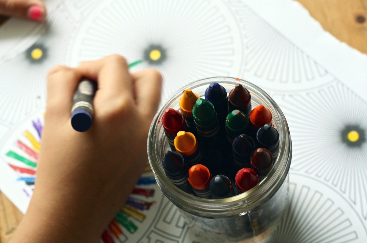 Child coloring a colorful picture. There is a glass jar of crayons.