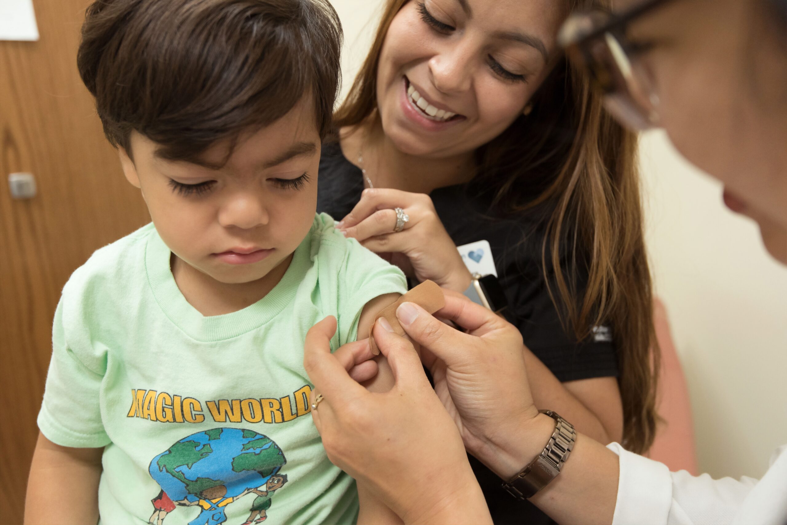 Child gets a band aid applied to his upper arm after receiving the influenza vaccine from his doctor and nurse
