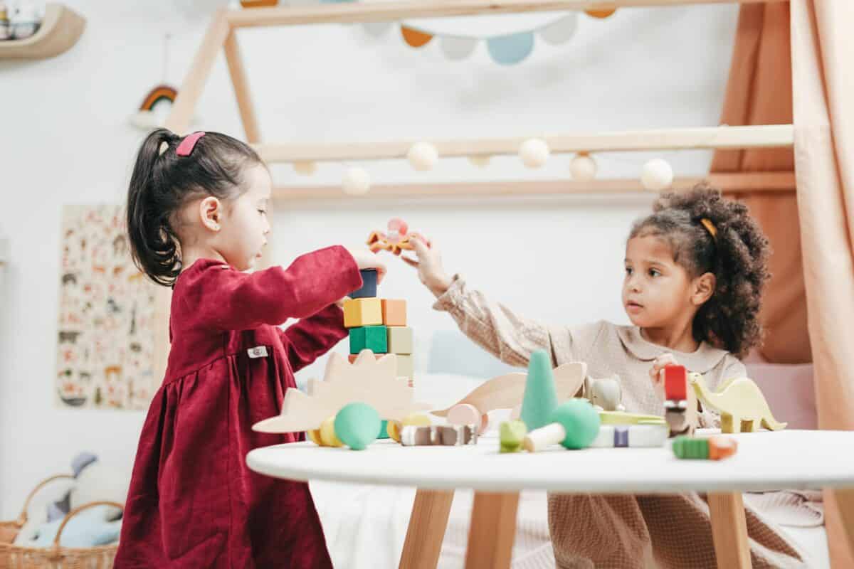 Two young girls play with blocks and other toys in an at-home daycare playroom