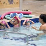 A group of children in a swimming pool with their female swim instructor