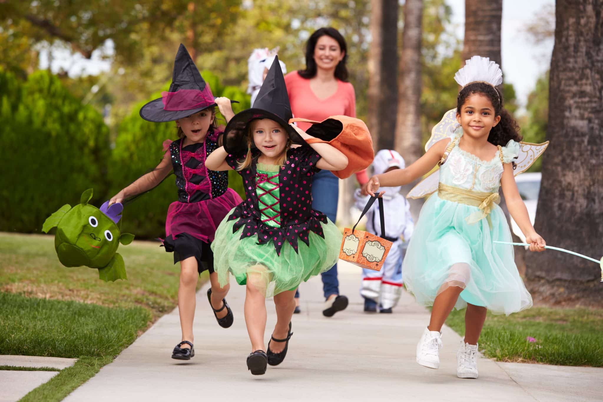 3 girls dressed in halloween costumes trick or treating with the mom trailing behind