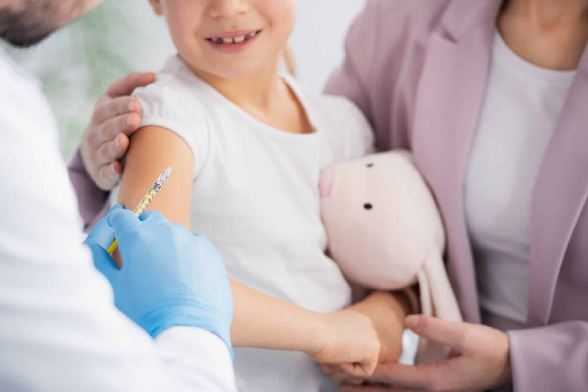 Doctor about to administer a vaccine to a child holding their mother and a stuffed animal